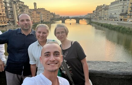 Zdjęcie przedstawia selfie zespołu podczas wieczornego spaceru po mieście. W tle rzeka i zachód słońca.